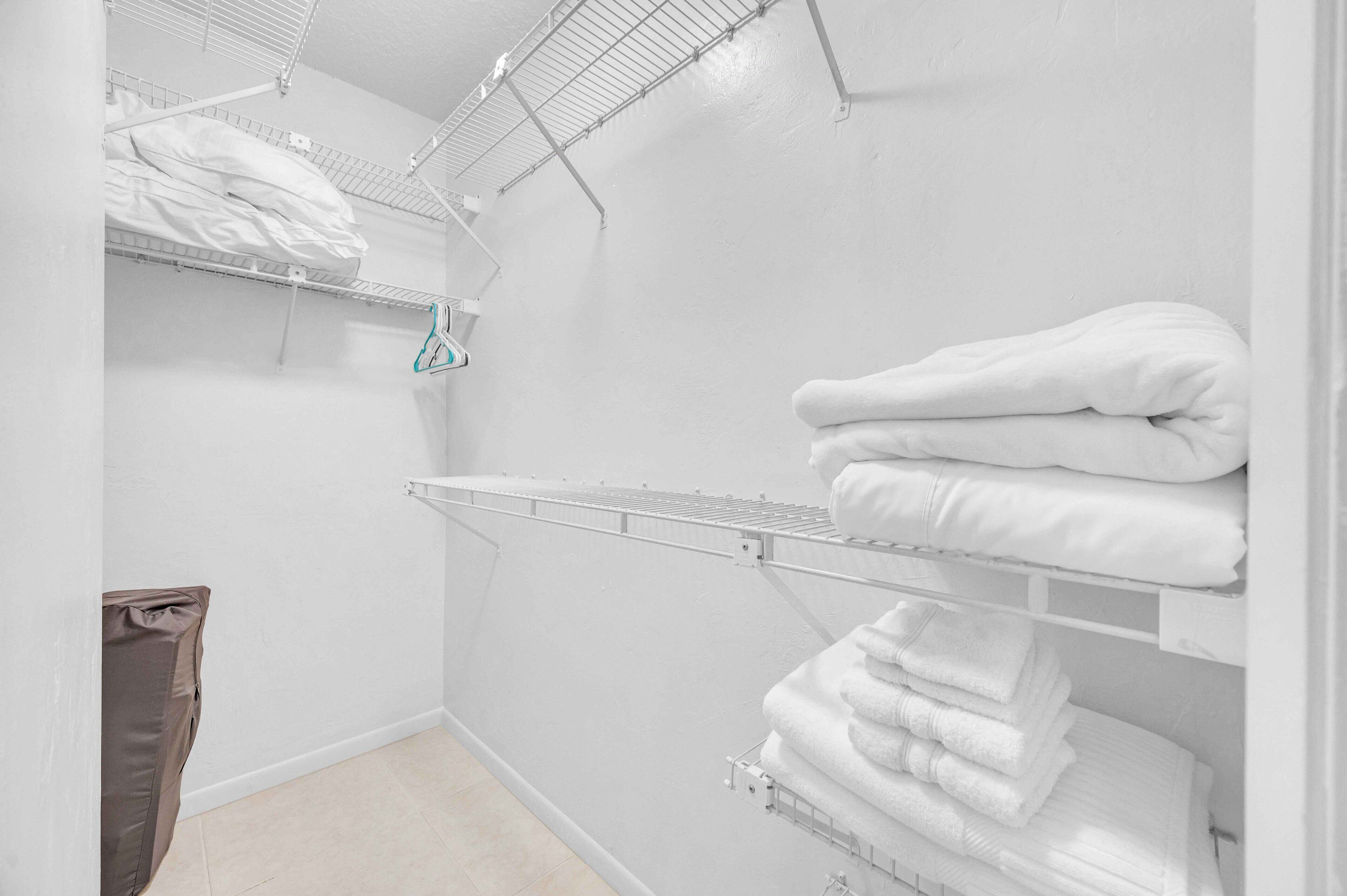 A white closet with shelves holding folded towels and a hanging rack.