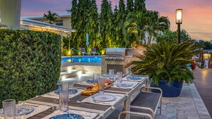 An outdoor dining area with a pool, grill, and lounge chairs.