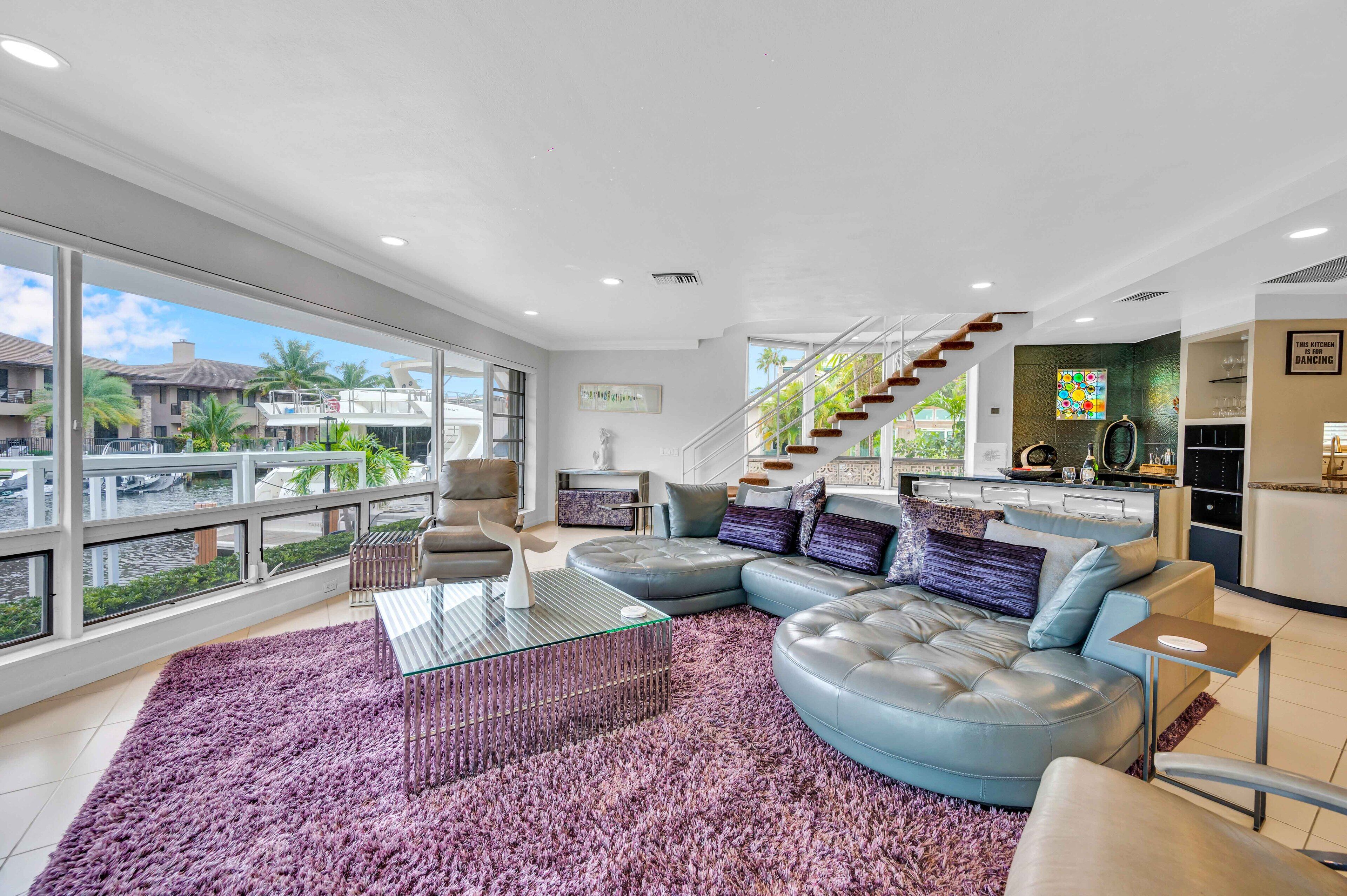 A modern living room with a large glass coffee table, a plush purple rug, and a curved sectional sofa.