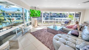 A spacious living room with a large glass window, a comfortable sofa, a coffee table, and a TV mounted on the wall.