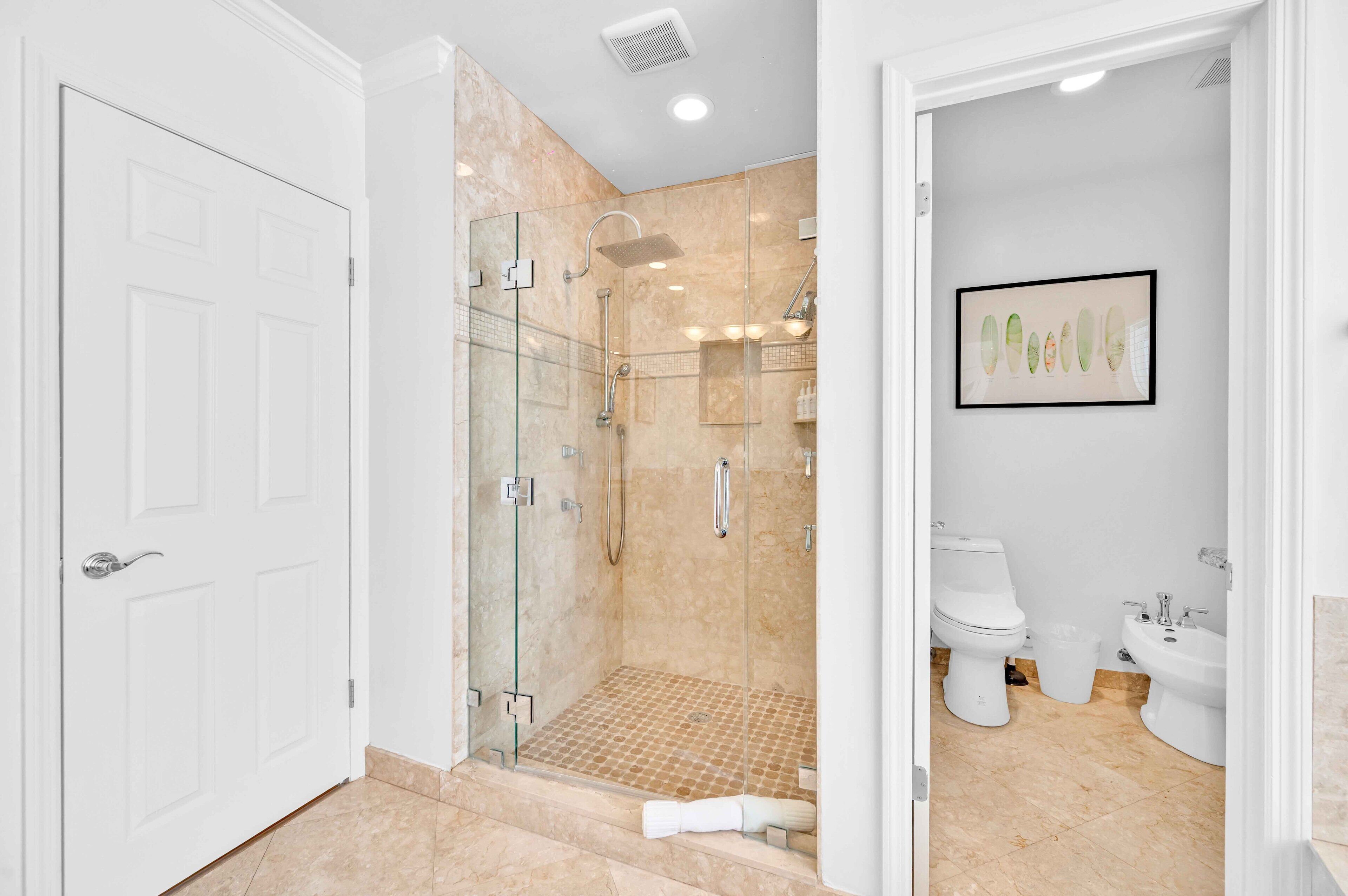 A modern bathroom with a glass-enclosed shower, a toilet, and a bidet.