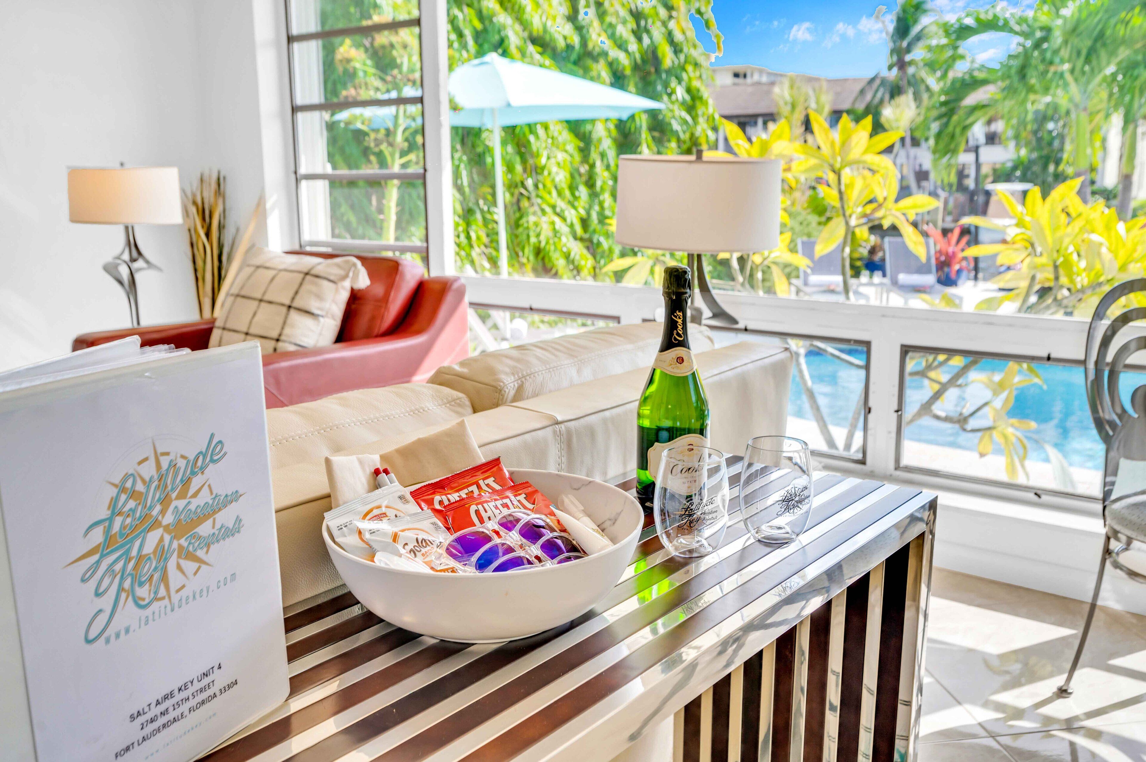 A hotel room with a pool view, a bottle of champagne, snacks, and a glass.