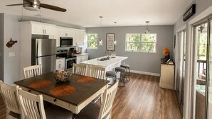 Une cuisine moderne avec des meubles blancs, un îlot central et un coin repas comprenant une table et des chaises en bois.
