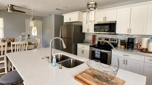 Une cuisine moderne dotée d’un grand îlot central, d’appareils électroménagers en acier inoxydable et de luminaires suspendus.