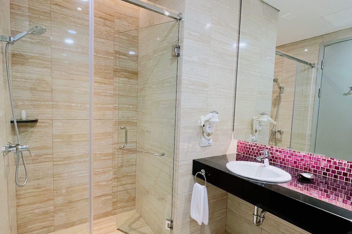 Een moderne badkamer met een douchecabine van glas, een zwart aanrechtblad en een backsplash van roze mozaïek.