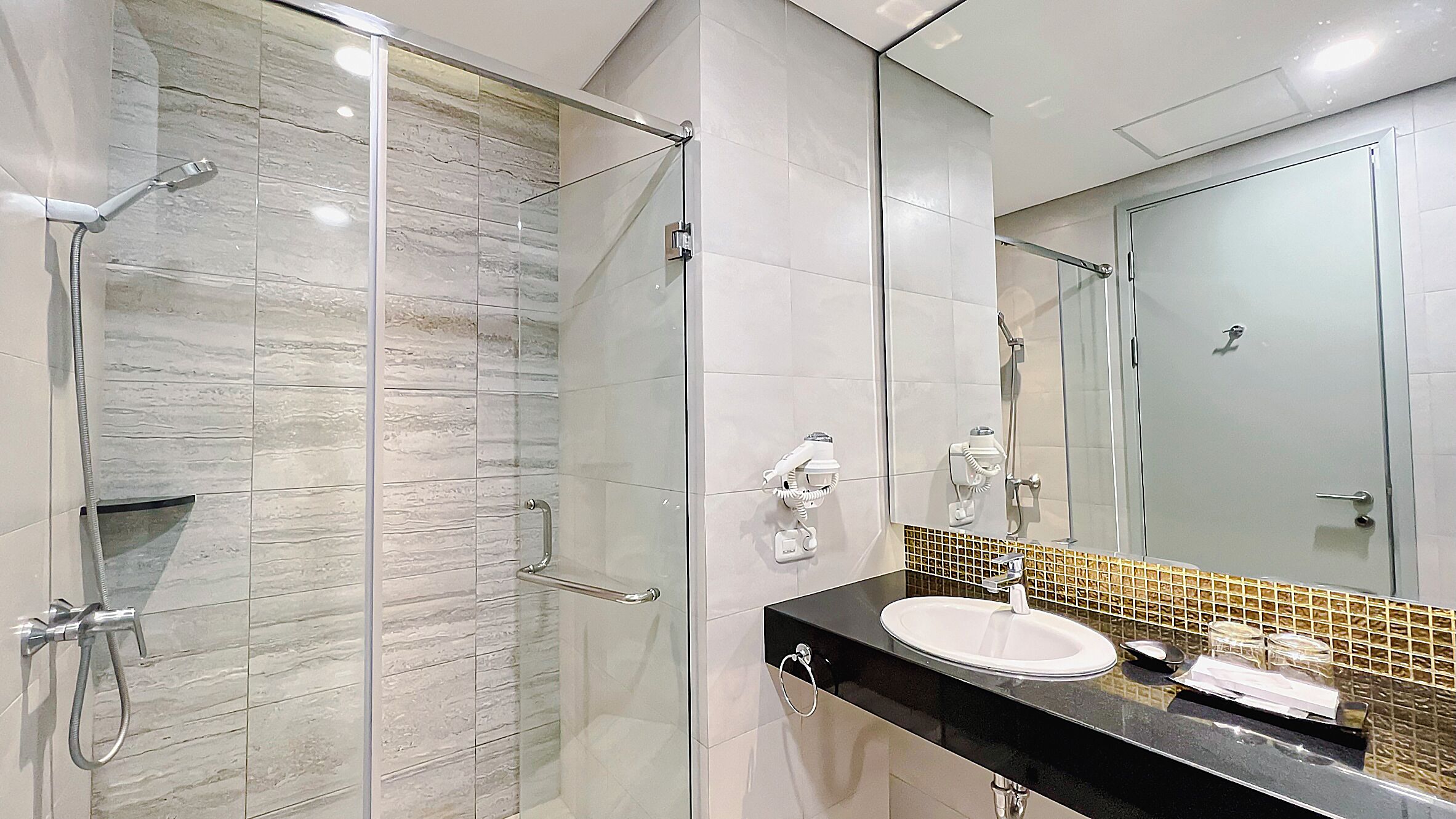 A modern bathroom with a glass shower enclosure, a black countertop, and a white sink.