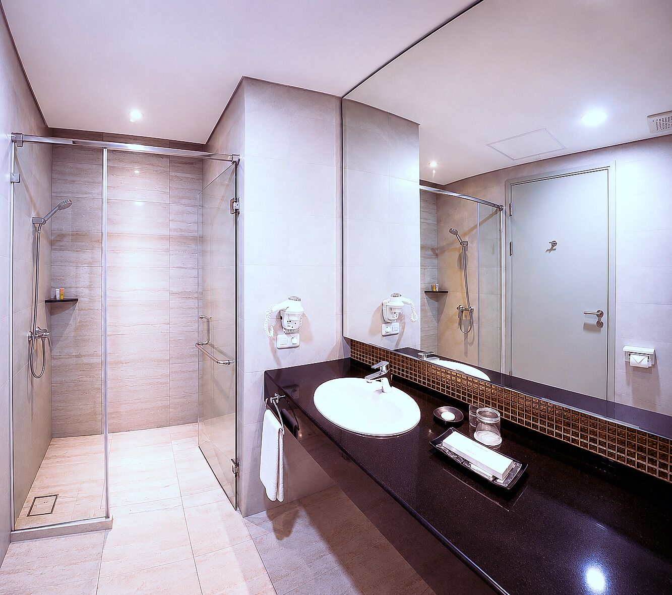 A modern bathroom with a glass-enclosed shower, a large mirror, and a dark countertop.