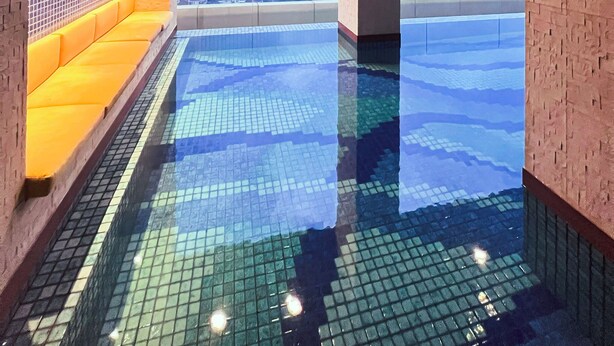 Une piscine à débordement située sur le toit, offrant une vue sur la ville, un espace détente avec des coussins jaunes et un sol carrelé.