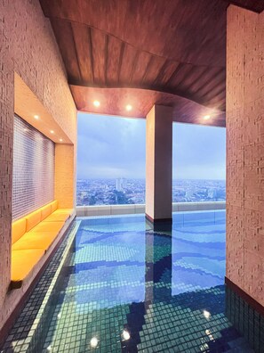 A rooftop infinity pool with a city view, a seating area with yellow cushions, and a tiled floor. - Leedon Hotel & Suites Surabaya (Surabaya)