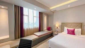 Une chambre d’hôtel avec un lit, une banquette, une table de chevet et une fenêtre avec des rideaux.