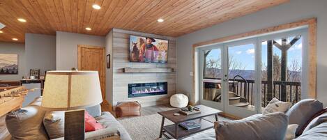 A cozy living room with a fireplace, comfortable seating, and a large window offering a scenic view.