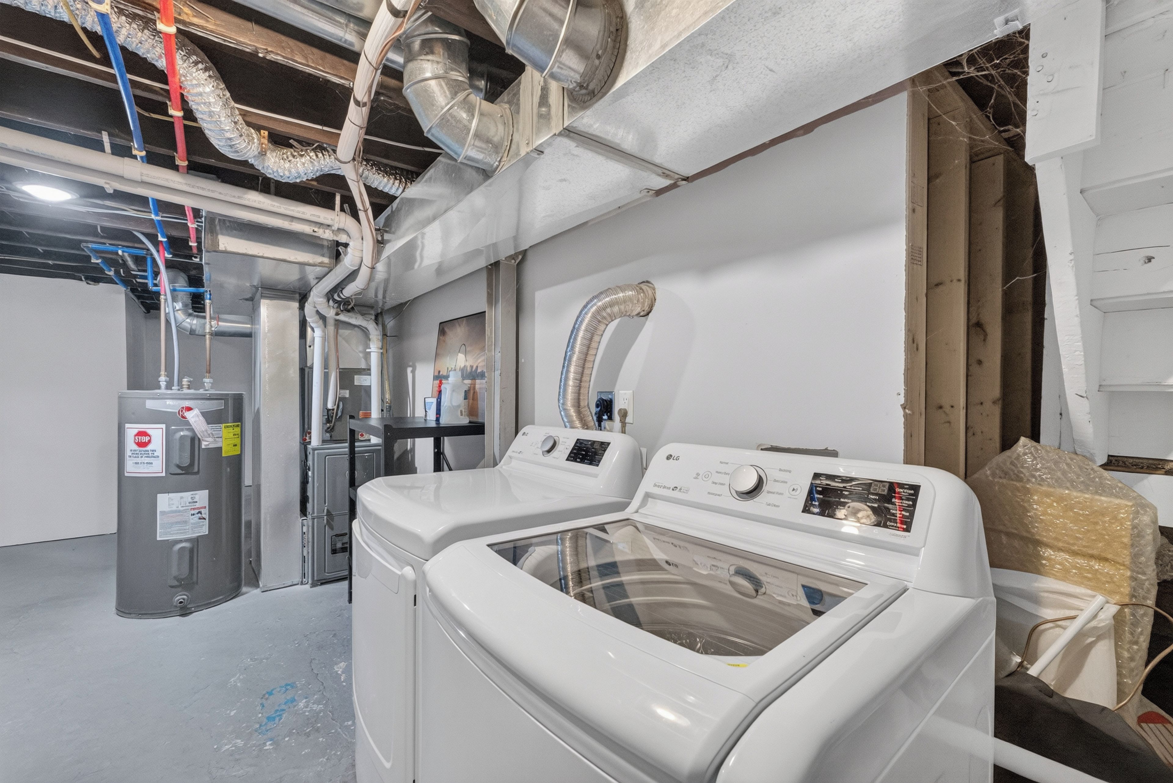 A laundry room with two front-loading washing machines, a utility room with a water heater, and visible ductwork on the ceiling.
