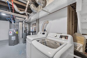 A laundry room with two front-loading washing machines, a utility room with a water heater, and visible ductwork on the ceiling.