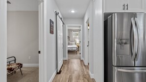 Une cuisine avec un réfrigérateur en acier inoxydable, un plancher en bois et des murs blancs.