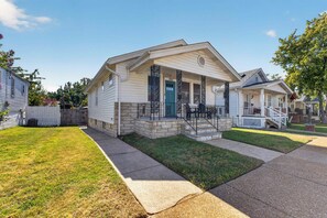 A single-story house with a front porch, a stone foundation, and a picket fence.