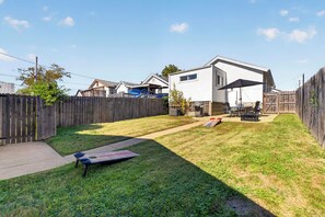 Un patio trasero con cerco de madera, un área de patio con mobiliario exterior y una casa al fondo.