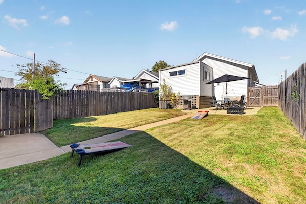 A backyard with a wooden fence, a patio area with outdoor furniture, and a house in the background.