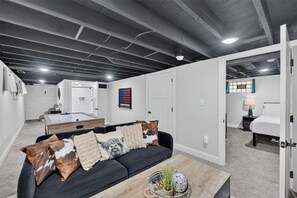 A modern living room with a black sofa, a coffee table with decorative items, and a view into another room with a bed and a nightstand.
