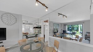 A modern kitchen with a glass dining table, a TV, and a view of the outdoors.