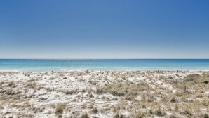 Una playa con arena, vegetación escasa, cielo despejado y aguas marinas tranquilas.