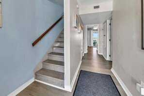 A hallway with a wooden staircase, light blue walls, and a gray carpet.