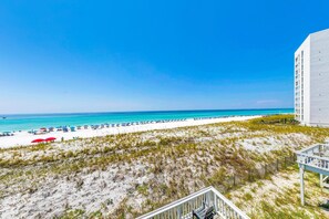 A beach view with a white building and a sandy area with grass. - Best time on the Beach - Southbay by the Gulf 129 - Private Patio | Walk to the Beach (Destin)