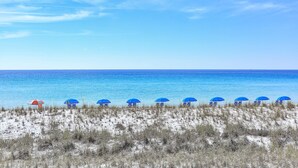 A beach with blue umbrellas and beach chairs, a sandy foreground, and a clear blue sky. - Completely Renovated 3-Bedroom Beach Front Townhome in Destin! (Destin)