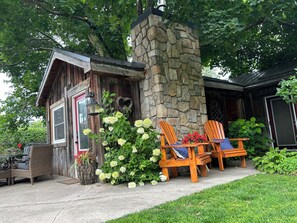 Una cabaña rústica con chimenea de piedra, fachada de madera y un área de descanso con sillas tipo Adirondack.