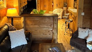 A cozy cabin interior with a wooden ceiling, a kitchen area, a dining space, and a living room with a leather couch and a coffee table. - Guest house close to Blue Mountain, Wasaga Beach and Collingwood!  (Nottawa)