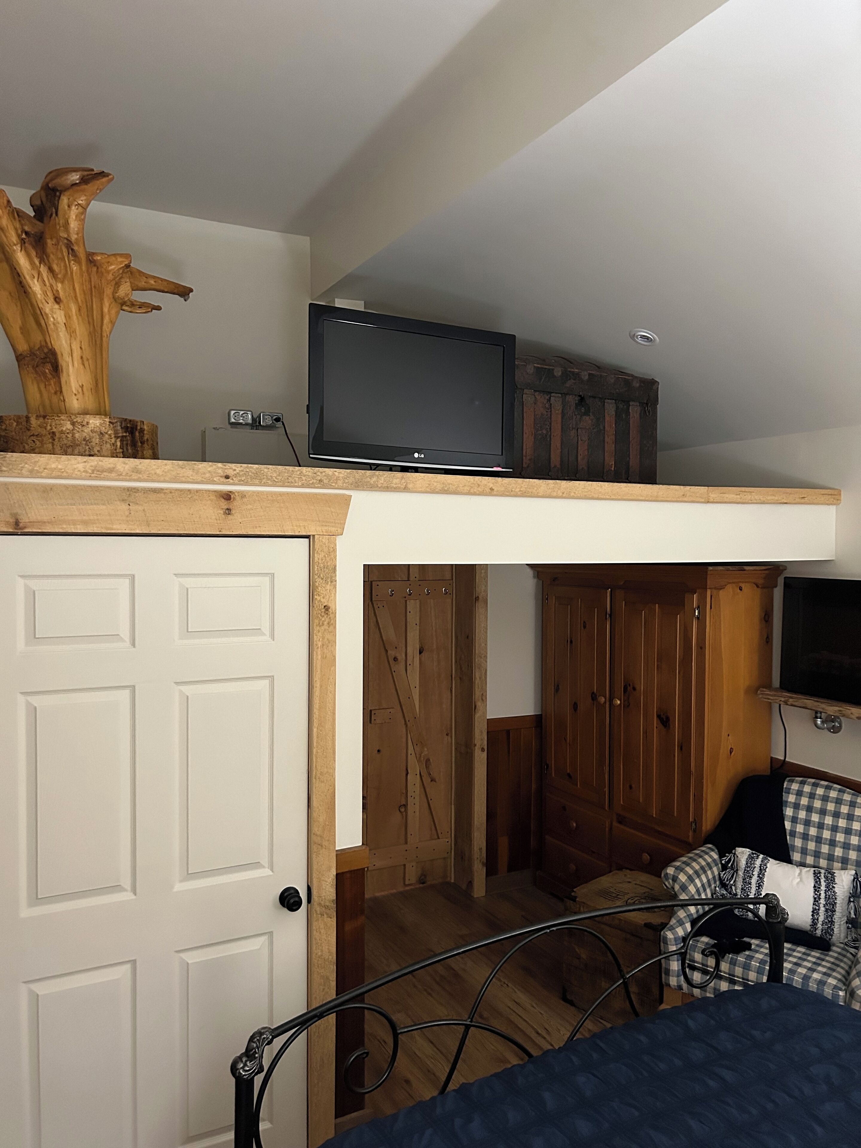 Une chambre à coucher avec un lit, un téléviseur posé sur une étagère, des armoires en bois et une porte.