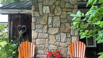 Two wooden Adirondack chairs with blue cushions, a stone wall, and a small table with a potted plant between them.