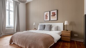 Un dormitorio con una cama grande, dos mesitas de noche con lámparas, un radiador y dos obras de arte enmarcadas en la pared.