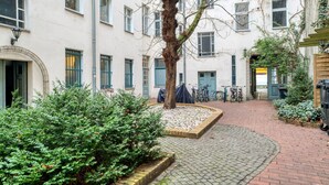 Un patio con un sendero adoquinado, un árbol y bicicletas estacionadas frente a un edificio con varias ventanas y puertas.