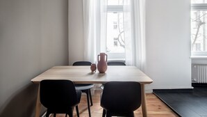 Un comedor minimalista con una mesa de madera, dos sillas negras y una jarrón de terracota.