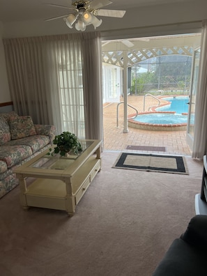 A living room with a sofa, coffee table, and a view of an outdoor swimming pool. - Quiet Private Guest House (North Fort Myers)