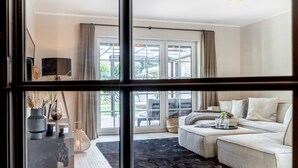 Ein modernes Wohnzimmer mit einem Ecksofa, einem Couchtisch und einem großen Fenster mit Vorhängen.
