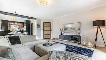 Ein modernes Wohnzimmer mit einer Eckcouch, einem Couchtisch, einem Flachbildfernseher und einem Essbereich mit Backsteinwand und Holzboden.