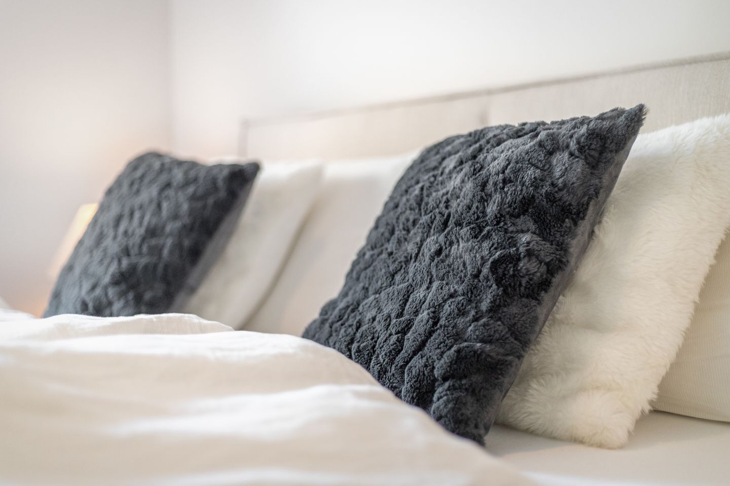 Ein Bett mit zwei Kissen, eines dunkel und eines hell, in einem Zimmer mit weißem Kopfteil.