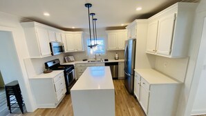 A modern kitchen with white cabinetry, a central island, stainless steel appliances, and a wooden floor.