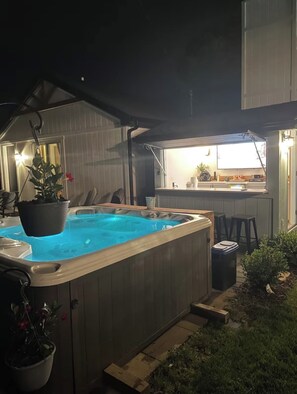 Ein Whirlpool in einem Garten mit Holzterrasse, einer kleinen Bar und Topfpflanzen.