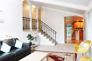 A living room with a black leather sofa, a yellow armchair, a staircase, and a kitchen in the background. - CHEERFUL 3 BEDROOM HOME WITH HUGE BACKYARD (Denver)