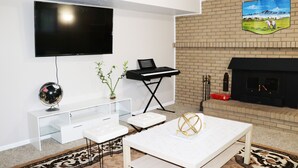 Uma sala de estar moderna com televisão de tela plana, lareira, piano e um globo em cima de um console branco.