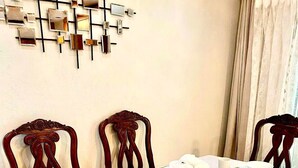 Uma sala de jantar com uma mesa branca posta para quatro pessoas, com jogos americanos dourados e pratos brancos.