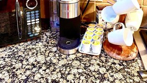 Cozinha com armários de madeira, micro-ondas, cafeteira e diversos utensílios sobre o balcão.