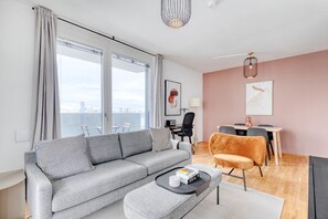 A modern living room with a grey sofa, a small coffee table, and a dining area with a table and chairs.