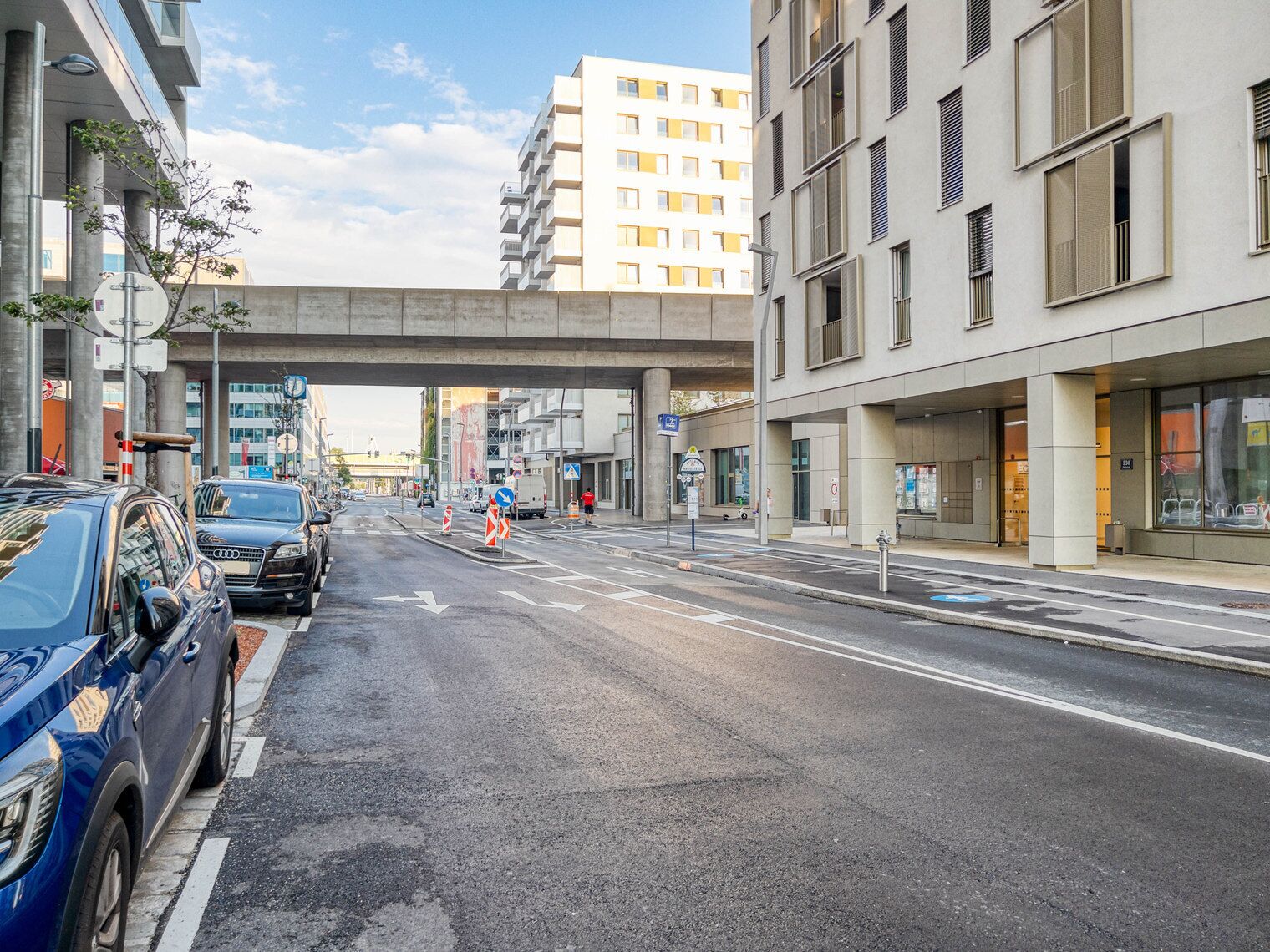 Een straat met geparkeerde auto's, een zebrapad en een gebouw met een modern ontwerp.