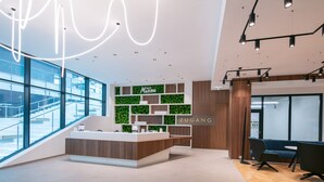 Ett modernt entréområde med en spiraltrappa i glas, en receptionsdisk och en sittgrupp med en blå soffa.
