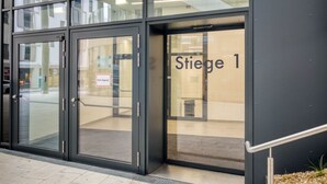 En modern entré till en byggnad med glasdörrar och en skylt med texten ”Trapphus 1”.