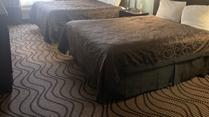 A hotel room with two beds, a nightstand with a lamp, and a patterned carpet. - La Plaza Inn & Suites (Freer)