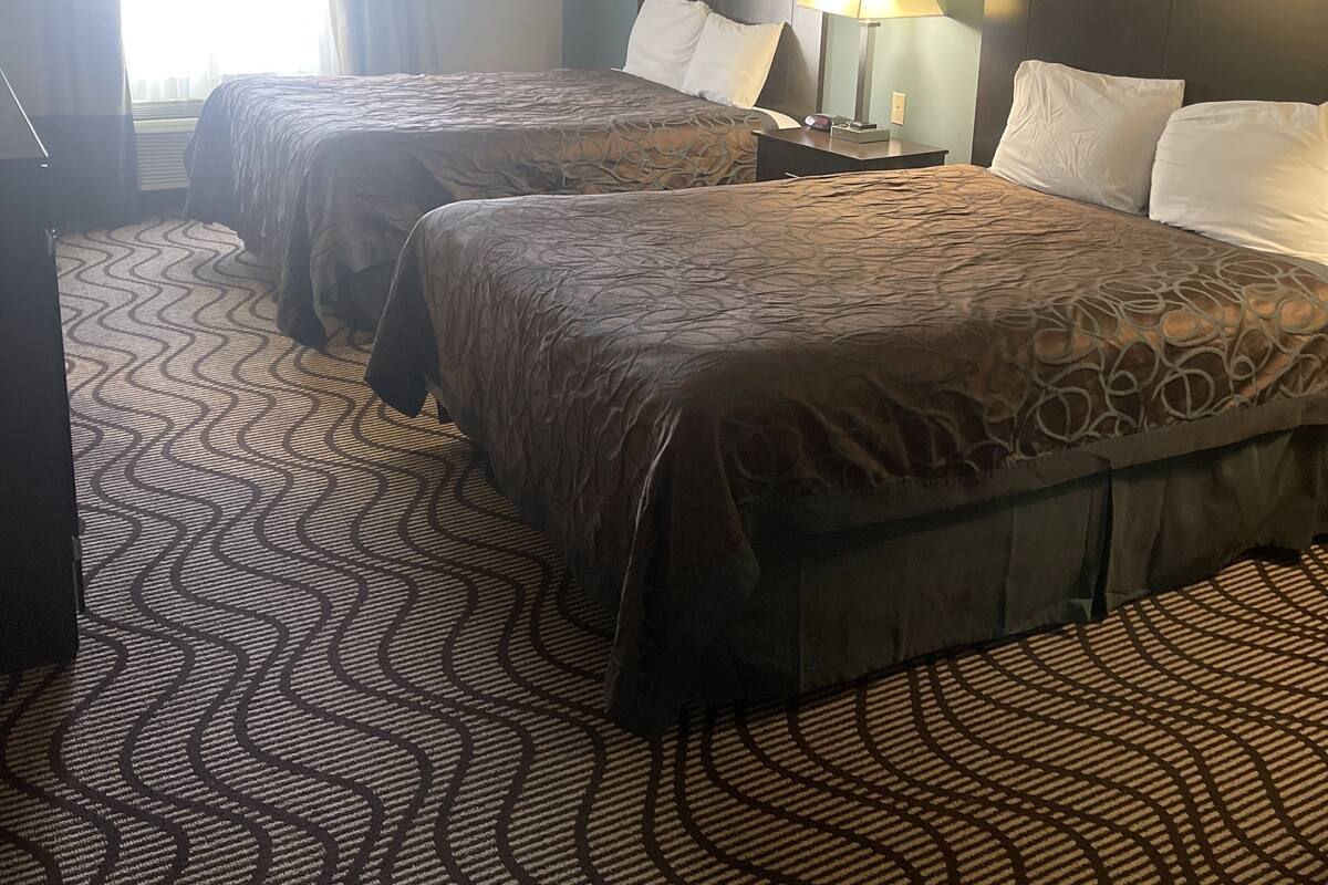 A hotel room with two beds, a nightstand with a lamp, and a patterned carpet.